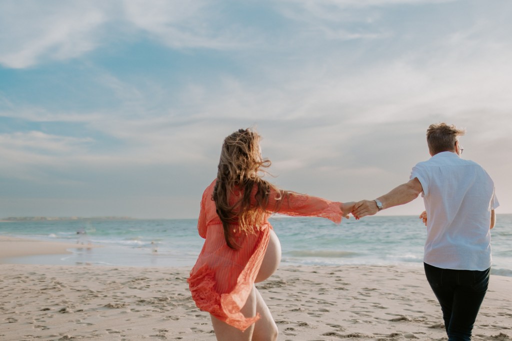 Pregnant woman and partner dance on the beach in Perth Western Australia